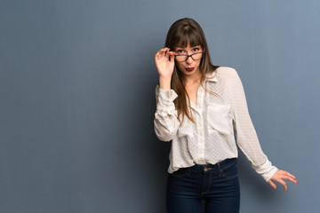 Woman with glasses over blue wall with glasses and surprised