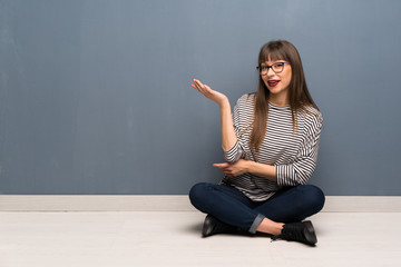Woman with glasses sitting on the floor holding copyspace imaginary on the palm to insert an ad
