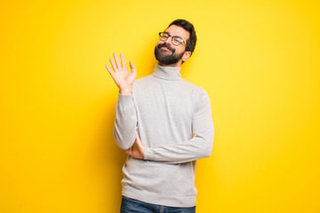 Man with beard and turtleneck saluting with hand with happy expression