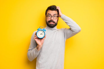 Man with beard and turtleneck restless because it has become late and holding vintage alarm clock - Powered by Adobe