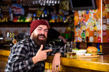 Pub is relaxing place to have drink and relax. Man with beard drink beer eat burger menu. Enjoy meal in pub. High calorie snack. Brutal hipster bearded man sit at bar counter. Hipster relaxing at pub