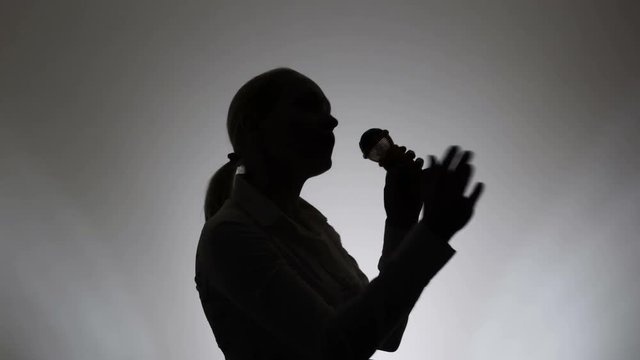Silhouette of a woman on a white background. A woman sings emotionally into a microphone.