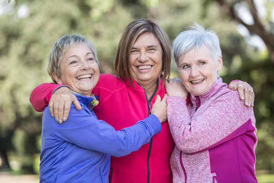 trio di  di amiche mature ridono felici vestite con tute colorate al parco
