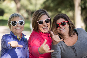 gruppo di 3 amiche mature ridono felici con occhiali da sole spiritosi - sfondo parco 