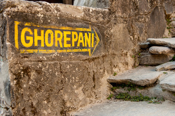 Yellow signpost arrow on the stone wall heading to Ghorepani on Poon Hill, Annapurna circuit trek, the trekking destination in Nepal, Himalayas.
