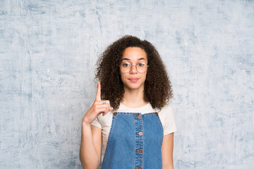 Dominican woman with overalls over grunge wall pointing with the index finger a great idea