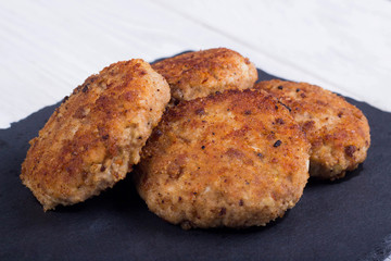 cutlets on a black flat plate, on a white wooden background