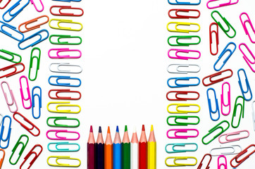 Many multi-colored stationery clips for documents and multi-colored pencils lie on a white background