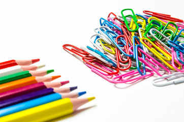Many multi-colored stationery clips for documents and multi-colored pencils lie on a white background