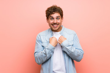 Blonde man over pink wall with surprise facial expression