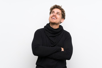 Blonde man over isolated white wall looking up while smiling