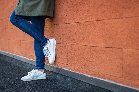 Woman wearing casual clothing and white sneakers leaning wall in city