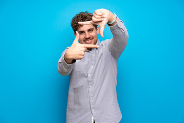 Blonde man over blue wall focusing face. Framing symbol