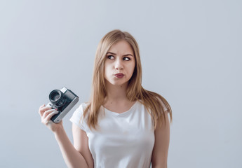 Fototapeta premium Attractive girl holding a vintage camera in her hands. Confusedly looks