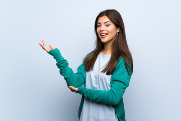 Teenager girl over blue wall extending hands to the side for inviting to come