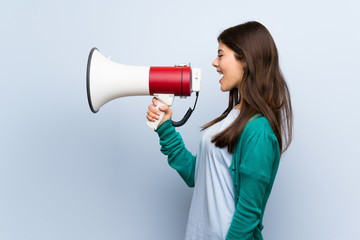 Naklejka premium Teenager girl over blue wall shouting through a megaphone