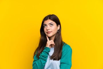 Teenager girl over yellow wall thinking an idea