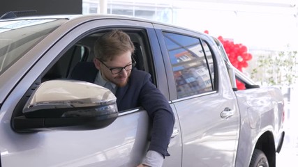 portrait of happy car buyer, smiling client man enjoy new automobile and shows keys sitting in cabin and looking through window at auto salon