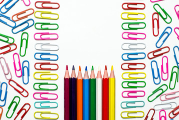 Many multi-colored stationery clips for documents and multi-colored pencils lie on a white background