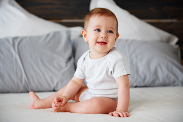 Smiling baby sitting on bed - obrazy, fototapety, plakaty