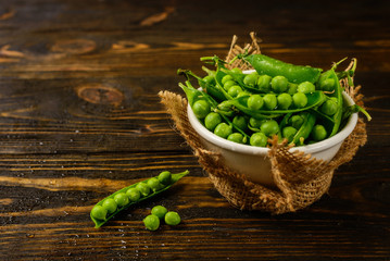 Pods of green peas and pea in bowl on a dark wooden background