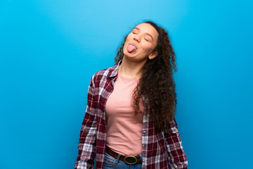 Teenager girl over blue wall showing tongue at the camera having funny look