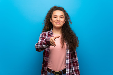 Teenager girl over blue wall shaking hands for closing a good deal