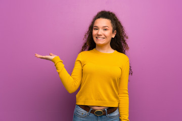 Teenager girl over purple wall holding copyspace imaginary on the palm to insert an ad