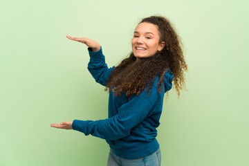 Teenager girl over green wall holding copyspace to insert an ad