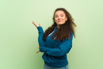 Teenager girl over green wall extending hands to the side for inviting to come