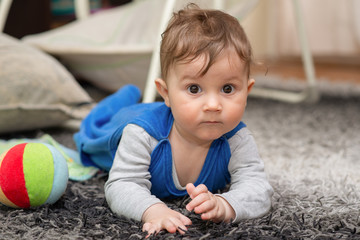 The boy lies on his stomach on the carpet and crawls