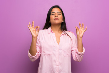 Young Colombian girl over purple wall in zen pose