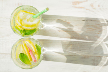 glass of homemade lemonade with lemons, mint and paper straws on wooden rustic background. Summer refreshing beverage. hard shadows
