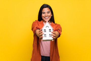 Young Colombian girl over yellow wall holding a little house