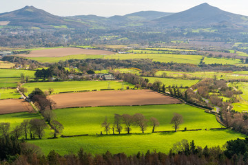 Stunning view from the top of the Carrickgollogan Hill, Ireland, after hiking in Dublin Mountains Way on a lovely spring day with colorful agricultural land patches and trees caressed by the sunlight.