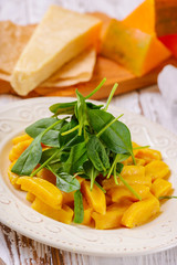 Tasty yellow pumpkin gnocchiwith spinach and parmesan cheese on a plate closeup. Decorated with edible flowers