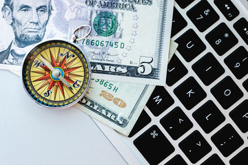 Financial online success concept. Compass and some dollars on a laptop keyboard.