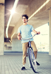 Naklejka premium people, style, leisure and lifestyle - young hipster man riding fixed gear bike on city street
