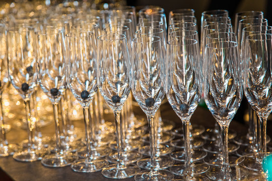 Closeup of many empty glasses for champagne with blueberry on bottoms inside of them. Horizontal color photography.