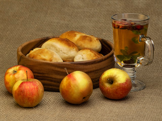 homemade apple patty in a wooden plate, herbal tea in a cup and apples on a linen tablecloth.