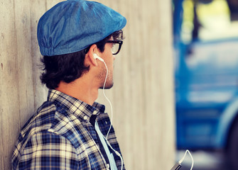 people, technology and lifestyle - happy young hipster man with earphones and smartphone listening to music
