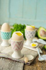 Boiled eggs in holders with avocado on a grey wooden rustic table