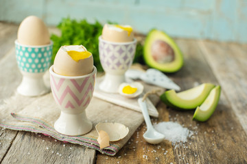 Boiled eggs in holders with avocado on a grey wooden rustic table
