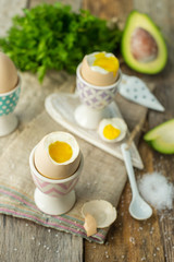 Boiled eggs in holders with avocado on a grey wooden rustic table