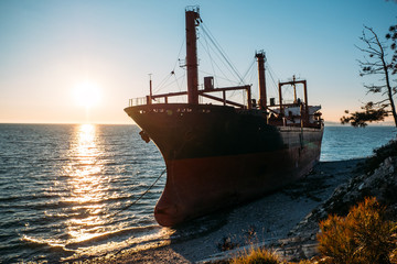Fototapeta premium Large iron cargo ship run aground at sea bay. Industrial sea vessel shipwreck on coastline after storm accident