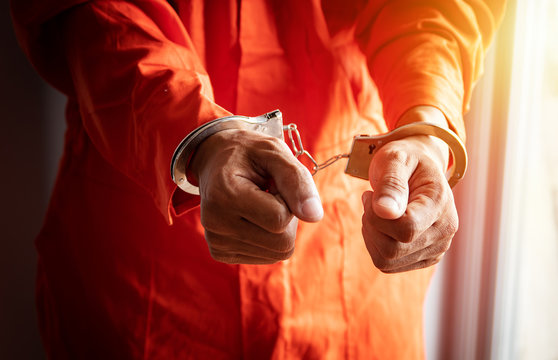 close up of prisoner's hands with handcuffs in orange jumpsuit at prison