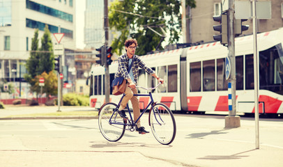 people, style, leisure and lifestyle - young hipster man with shoulder bag and earphones riding fixed gear bike on city street