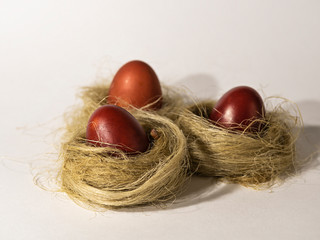 Three Easter red eggs in nests on a light background.