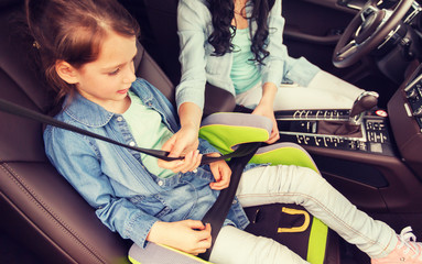 family, transport, road trip and people concept - happy woman fastening child with safety seat belt in car