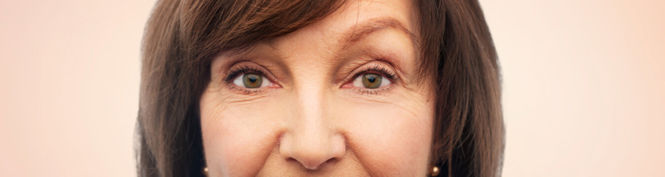 beauty, vision and old people concept - half of face of senior woman over beige background